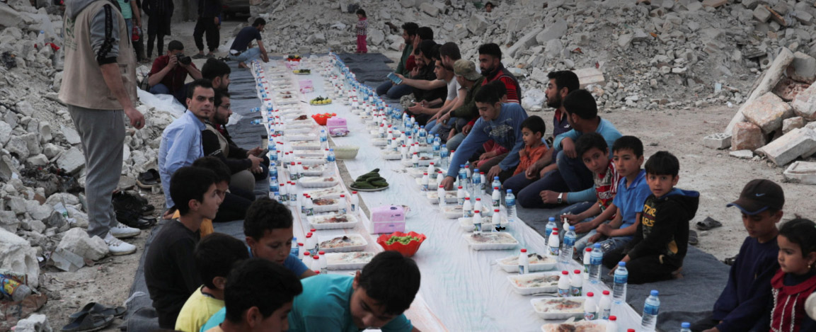 Syrian civilians eat an Iftar meal provided by a group of volunteers in a damaged neighborhood of Atarib, Aleppo countryside, amid fears of the COVID-19 virus in Syria..