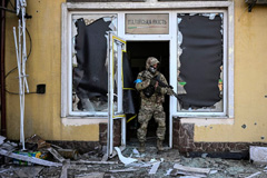 soldier with gun in a shattered doorway with debris and glass everywhere, Aris Messinis/AFP via Getty Images