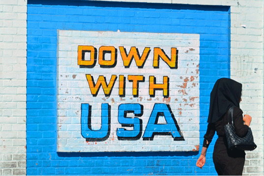 An Iranian woman walking past a wall that says Down with USA