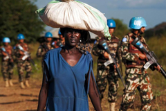 A displaced woman carries goods as United Nations Mission in South Sudan peacekeepers patrol outside the premises of the UN Protection of Civilians site in Juba on October 4, 2016.
