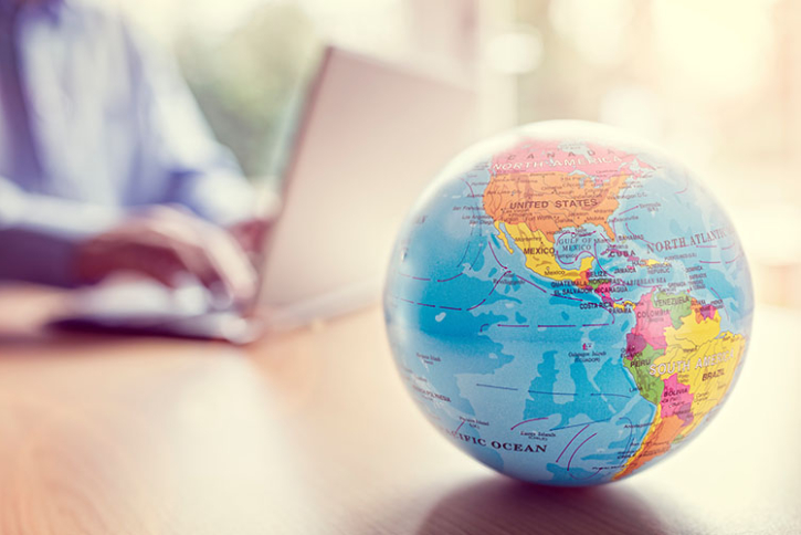 A globe in the foreground with a person working on their laptop in the background