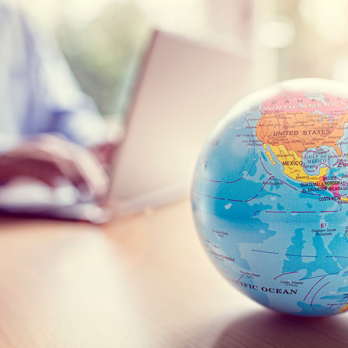 A globe in the foreground with a person working on their laptop in the background